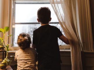 Two young children looking out window at the cold