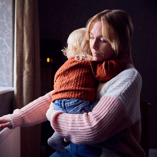 Young mum holding young child beside a radiator
